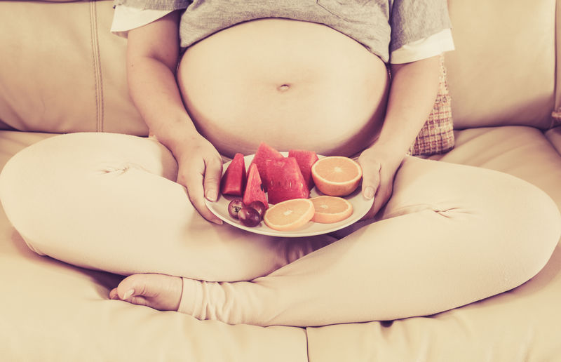 孕妇坐在沙发上拿着一盘水果