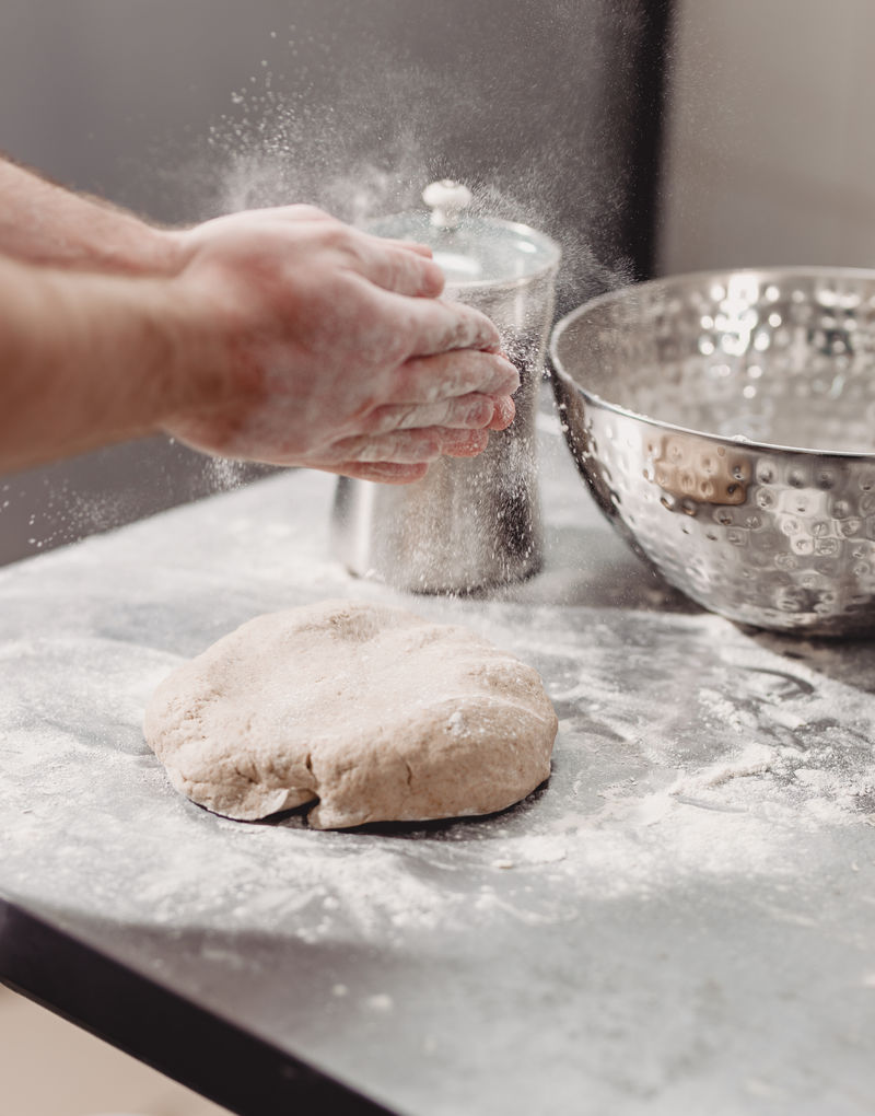 面包师在面包房的桌子上往面团里加面粉