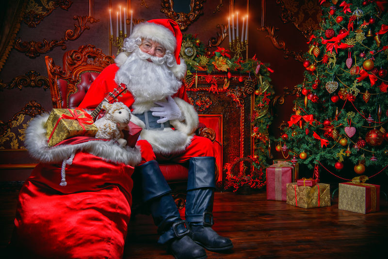 在壁炉旁边的一间漂亮房间里-圣诞老人惊喜地坐在圣诞树旁-手里拿着一袋礼物