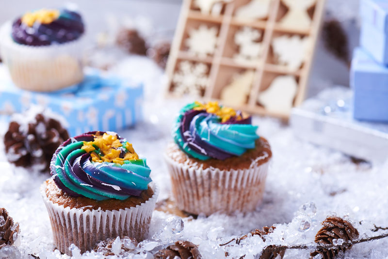 冬季纸杯蛋糕雪上有渐变奶油和金色星星背景是礼物木制玩具圆锥体和雪花冬情