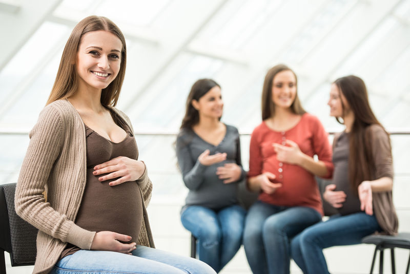 漂亮的孕妇正在看照相机-快乐的孕妇在医院的产前班上聊天