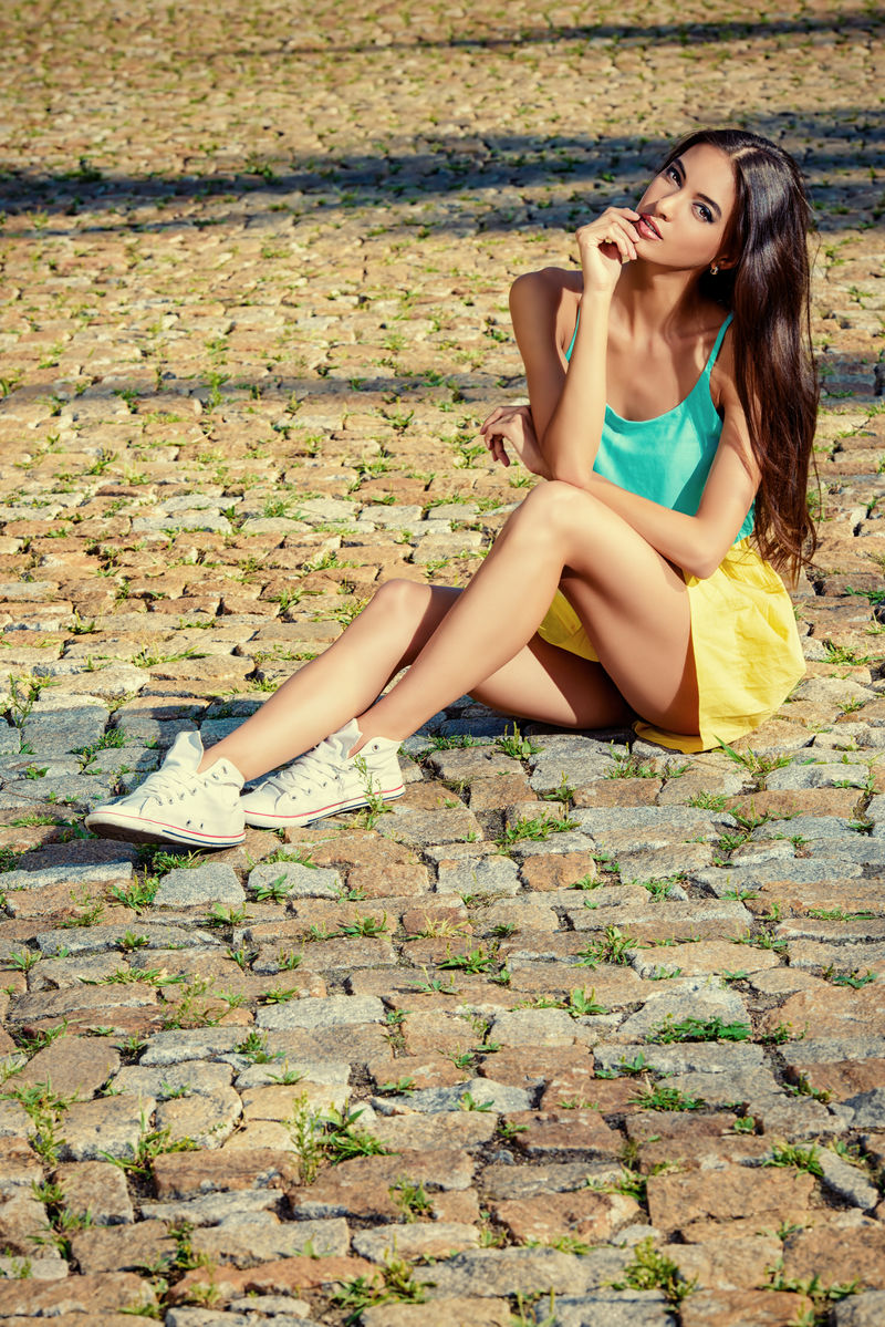 穿着休闲夏装的漂亮年轻女子坐在铺好的路上时尚镜头