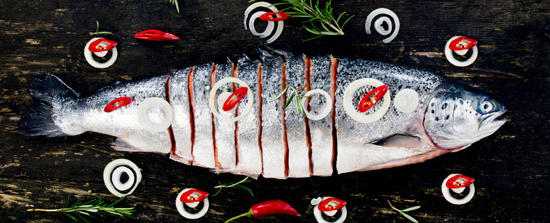 生鲑鱼配柠檬香草和香料放在深色粗木板上