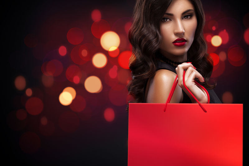 购物的女人拿着红色的袋子在灯光背景虚化在黑色星期五的圣诞假期的背景