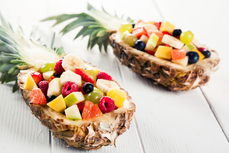 在一张白色的木桌上用凤梨船在夏季特写两套新鲜水果沙拉