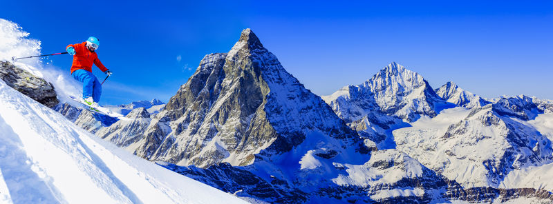 人从岩石上跳下来在铺着垫子的新鲜雪粉上滑雪