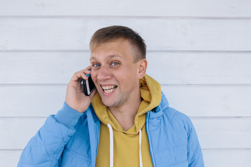 笑的年轻人在打电话在白木背景下使用智能手机的人