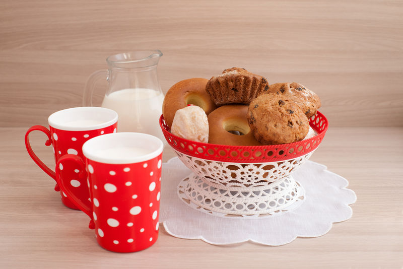 红调的早餐-牛奶在明亮的杯子和柳条花瓶白色餐巾加舒适