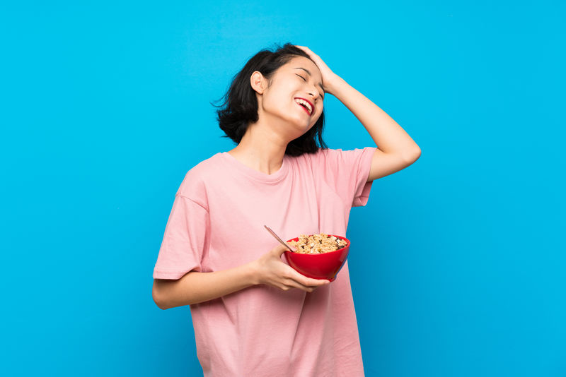 亚洲年轻女子拿着一碗谷类食品意识到了一些事情并打算解决这个问题