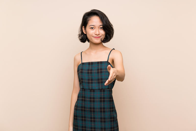 亚洲年轻女子翻过隔离的黄墙为成交而握手