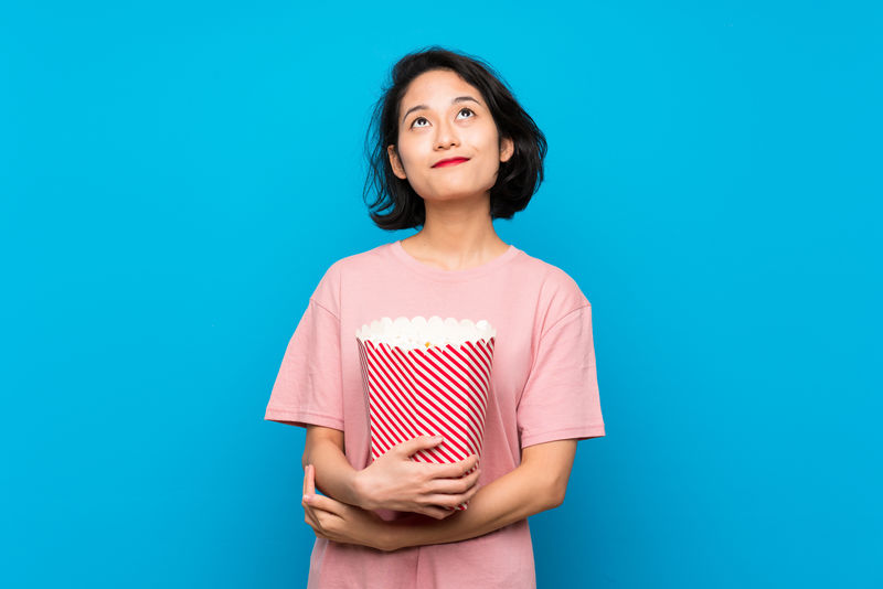 亚洲年轻女子一边吃着爆米花一边笑着抬头看