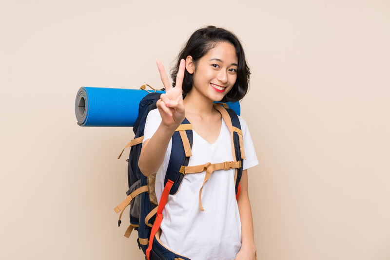 亚洲女旅行者在孤立的背景上微笑并展示胜利标志