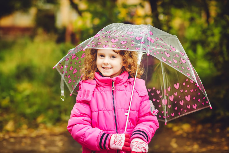 秋天公园里躲在雨伞下的小女孩