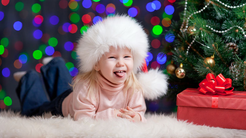 穿着圣诞帽的女婴带着礼物躺在圣诞树旁