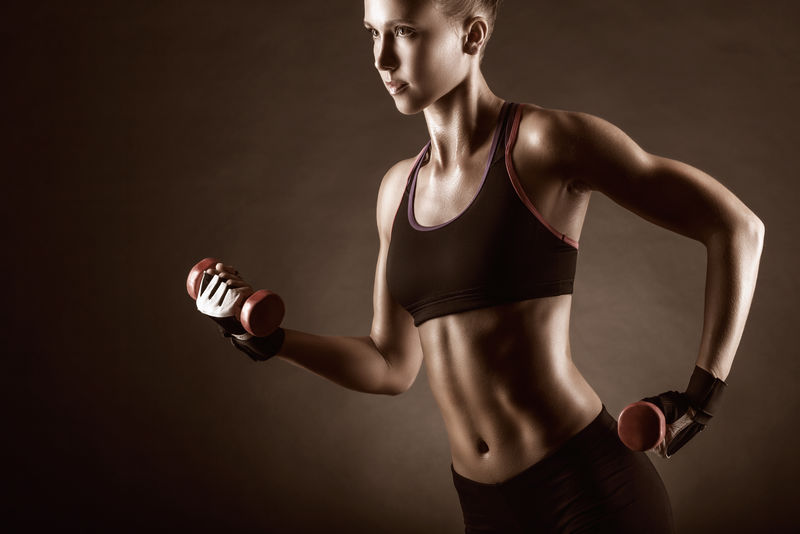 身穿哑铃的健美女子在黑暗的背景下
