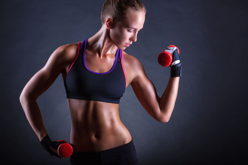 在黑暗的背景下玩重量的年轻女子