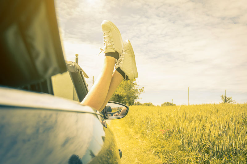 穿着鞋子的年轻酷女孩从汽车窗外欣赏夏天的景色