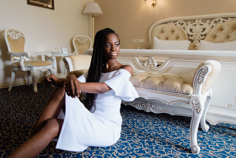 在豪华的欧洲酒店里有魅力的非洲女人模特坐在铺着蓝色地毯的地板上她把手放在膝盖上酒店客房采用古典风格设计