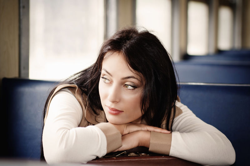 一个浅褐色的女孩坐在火车上提着一个手提箱