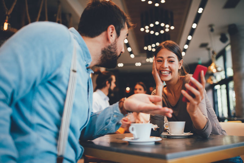 年轻的快乐夫妻在咖啡厅用智能手机