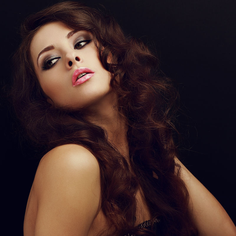 美丽的化妆女人-长卷曲的头发和粉红色的嘴唇往回看黑色背景-特写镜头