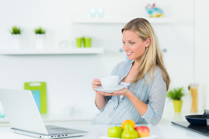 年轻漂亮的女人与笔记本电脑在厨房