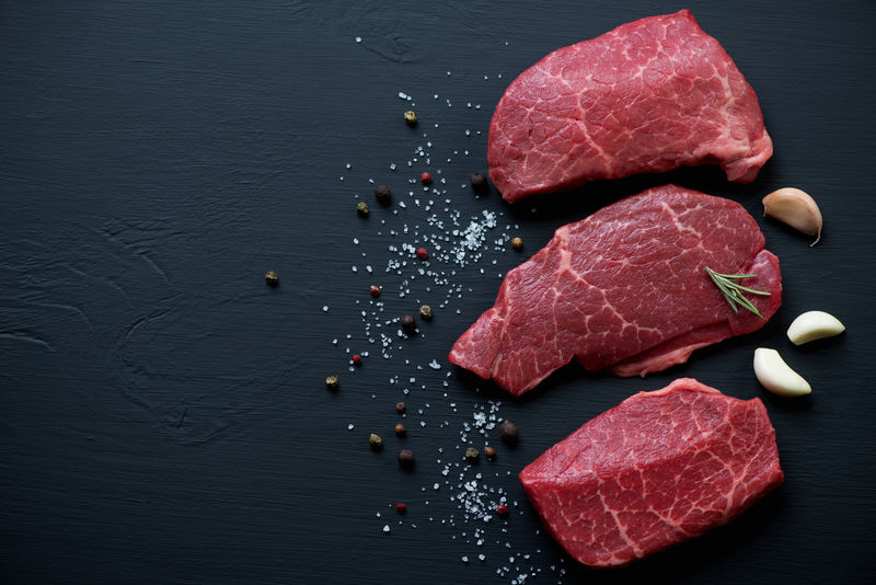 黑色木质表面上带有调味料的生大理石牛排