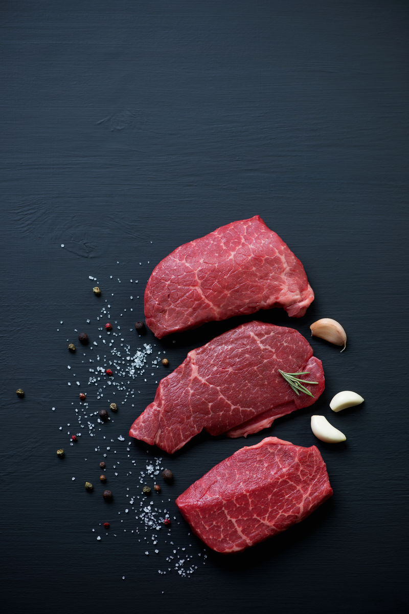 黑色木质表面的大理石牛排和调味料