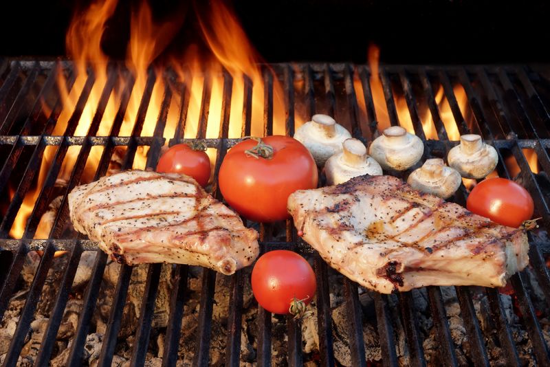 两块美味的肋排、蔬菜、西红柿、蘑菇-在燃烧的烧烤架上烹制而成-夏季野餐或烧烤聚会或野餐现场-没有人-黑色背景隔离