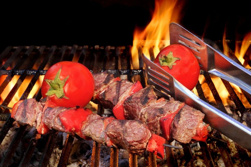 两个烤牛肉烤肉串和西红柿放在热腾腾的烤架上-野餐或户外聚会的美味小吃