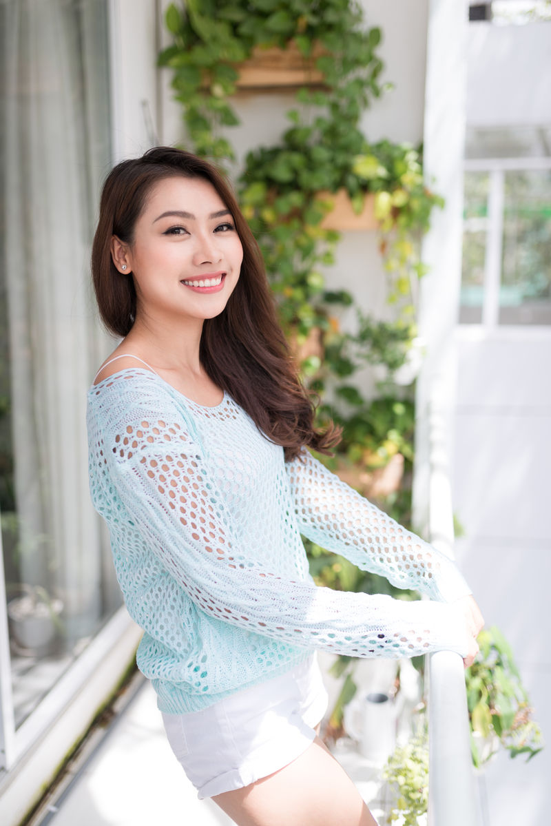 年轻的亚洲妇女在阳台上休息，享受新鲜空气。