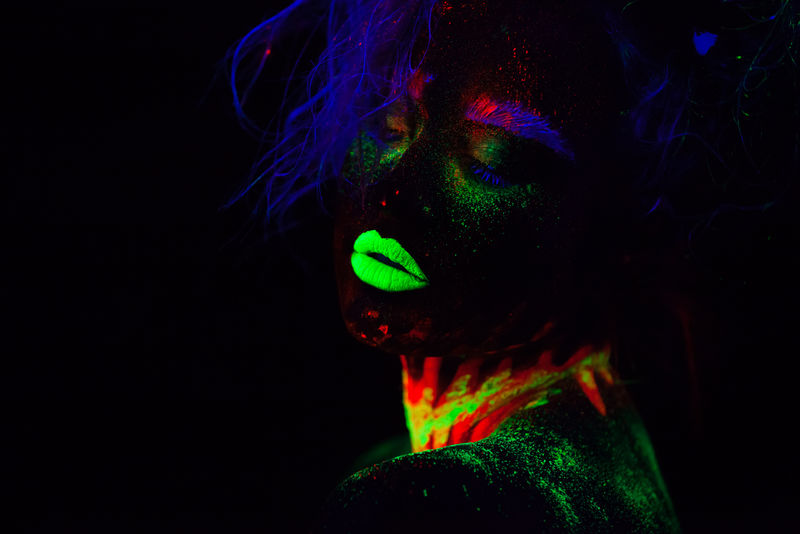 美丽的外星模特,蓝色头发,绿色嘴唇,霓虹灯下。它是一幅荧光彩妆的美丽模特的近照,是一幅彩色的女性在紫外光下摆姿势的艺术设计。