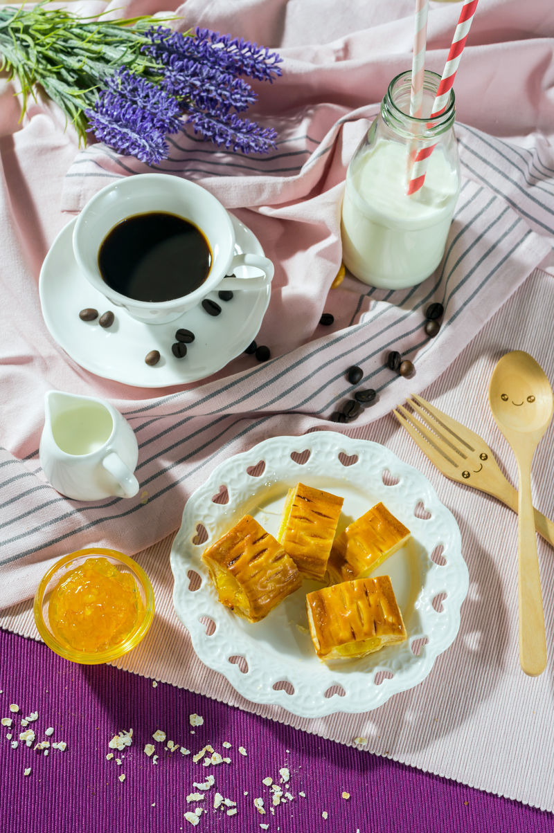 早餐套餐。桌子上的果酱馅饼，配咖啡杯，杯子和瓶子里的白牛奶，俯视图，健康食品理念。