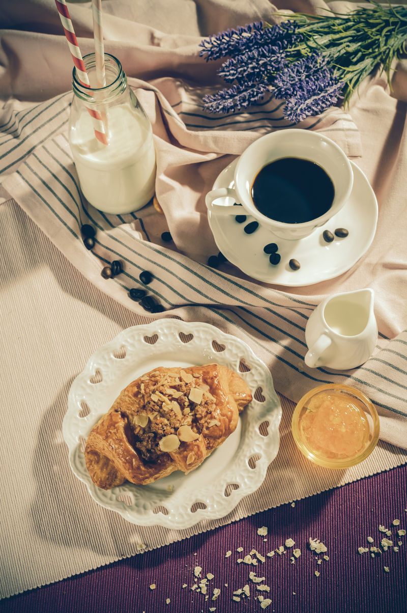 早餐套餐。餐桌上的面包盘上有果酱，咖啡杯上有白牛奶，杯和瓶，俯视图，健康食品概念，复古色调。