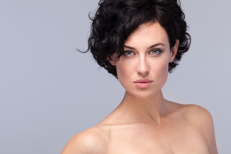 美丽女性的特写肖像,灰色背景上有短发卷曲。