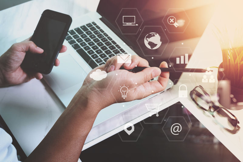 商人在现代办公室的木制办公桌上使用智能手机和笔记本电脑，带有虚拟图标界面