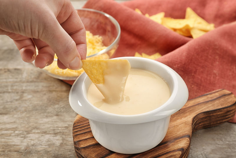 女用手蘸Nacho在碗里蘸啤酒奶酪，特写