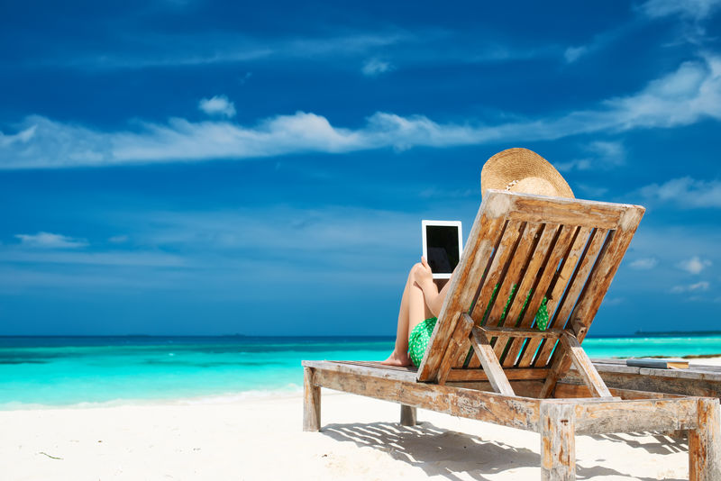 海滩上戴着平板电脑的戴帽子的年轻女子