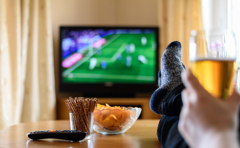 电视、看电视（足球赛）-脚放在桌子上-还有大量的小吃-库存照片