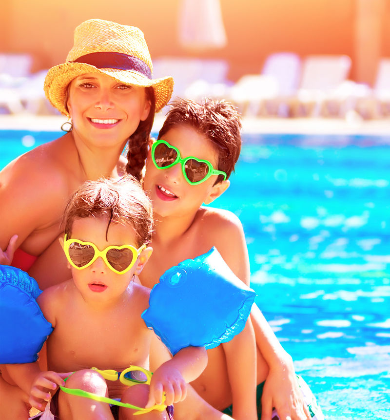 暑假快乐家庭-带着两个可爱孩子的年轻母亲在海滩度假胜地的游泳池旁玩耍-爱与友谊的概念