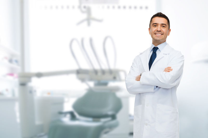 医疗保健、职业、口腔医学和医学概念-在医疗办公室背景下微笑的中年男性牙医