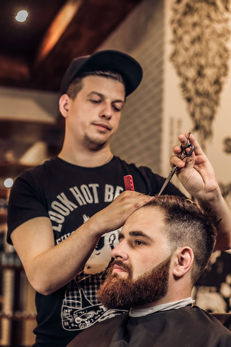 小胡子男人在理发店被理发师剪胡子的特写侧视图。坐在理发店的椅子上，保持完美的身材。真正男人的打扮。