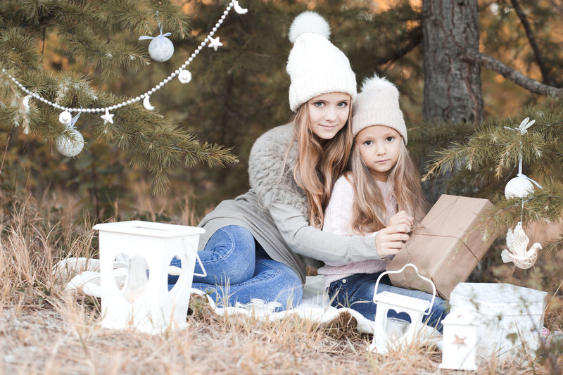 微笑的女孩坐在户外的圣诞装饰品。看着摄像机。开玩笑的。打开圣诞礼物。