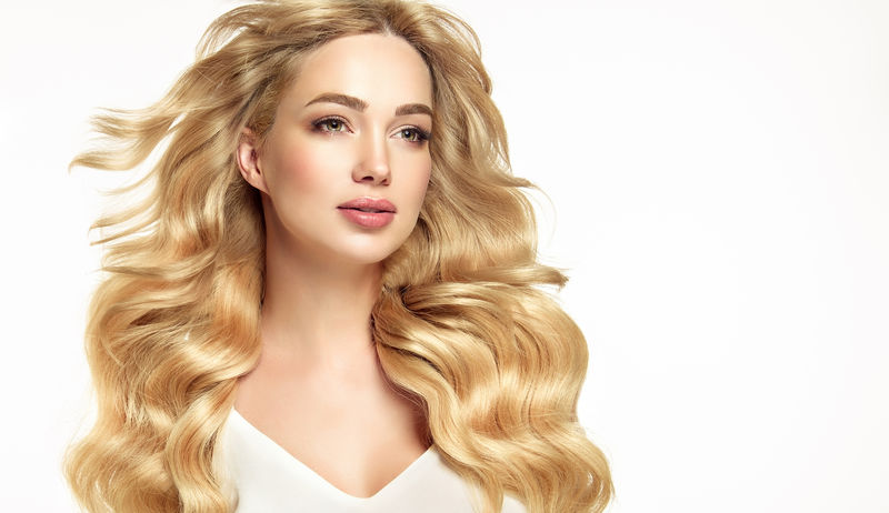 金发碧眼的女孩，长而闪亮的卷发。美丽的微笑的女性模特，卷曲的发型。