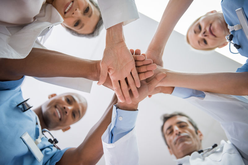 兴高采烈的多医生和护士们手拉手看着镜头-快乐的资深医生和年轻的护士们齐心协力-互相激励-团队合作和团结的理念