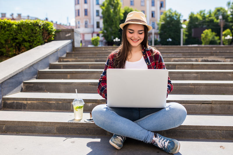 一个快乐的年轻女子坐在城市楼梯上，在室外使用笔记本电脑