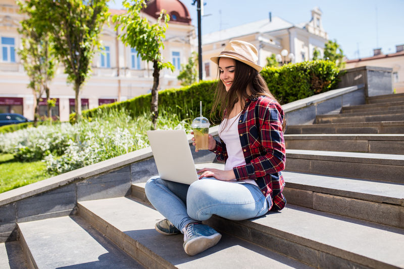 一个快乐的年轻女子坐在城市的楼梯上，在户外使用笔记本电脑