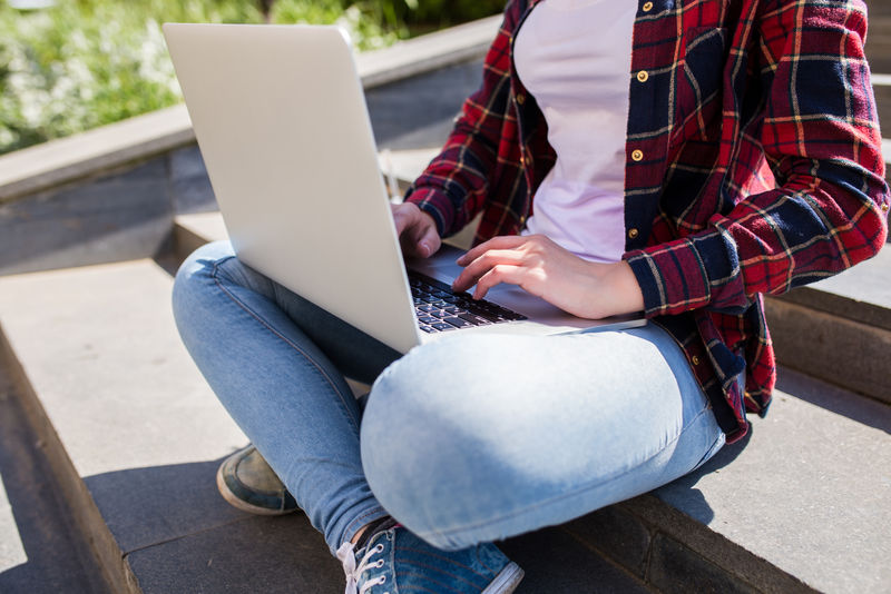 特写快乐的年轻女子坐在城市的楼梯上，在户外使用笔记本电脑