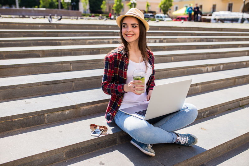 一个快乐的年轻女子坐在城市楼梯上，在室外使用笔记本电脑
