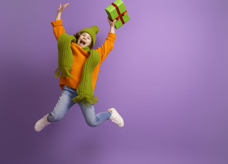 快乐的小女孩-在明亮的颜色背景上带着圣诞礼物-紫色、橙色和绿色